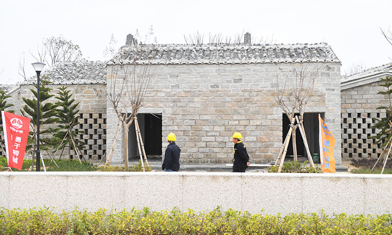 福平鐵路平潭一體化綜合交通樞紐由中鐵一局承建，匯集高鐵、公交、出租車、網(wǎng)約車、私家車等多種交通出行模式，為旅客提供“零換乘”和“無縫銜接”體驗。該交通樞紐采用“石頭厝”傳統(tǒng)民居形式，將平潭地方建筑特征與現(xiàn)代建筑功能相結(jié)合，合理運用自然采光和空氣通風原理。圖為12月7日，中鐵一局工人從福平鐵路平潭一體化綜合交通樞紐站前廣場“石頭厝”傳統(tǒng)建筑前經(jīng)過。（新華社記者 宋為偉 攝）