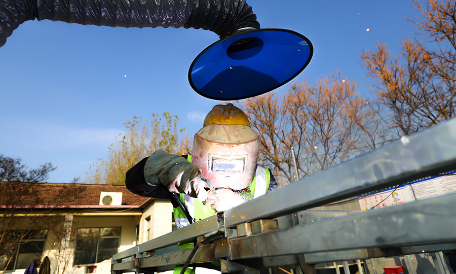 在施工過程中，項目綜合以往施工經驗結合施工工期，決定大膽采用裝配式安裝思路。首先建立龍骨骨架加工區，在加工區進行龍骨骨架整體框架的焊接加工，整個龍骨骨架長4.92米，高3.05米，經過加工區的焊接加固以及防銹處理后運輸到施工現場，通過螺栓、連接件以及角鋼進行現場組裝，組裝完成后利用叉車將龍骨骨架整體上墻，最后進行調平順坡這一道工序，保證了施工質量。圖為工人在進行龍骨骨架焊接。（范成濤 攝）