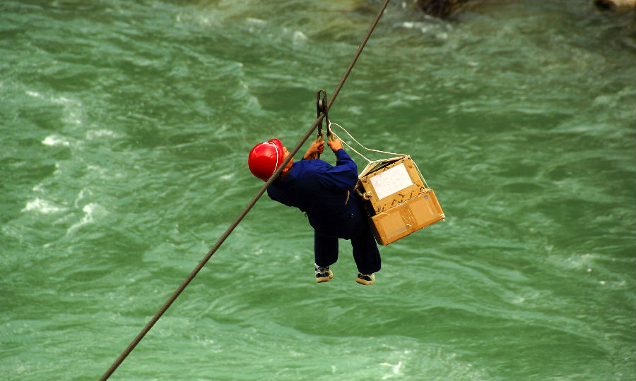 2007年，中國移動在獨龍江鄉(xiāng)開展“村通工程”，實現(xiàn)“村村通電話”。圖為移動員工用溜索運送建站物資。