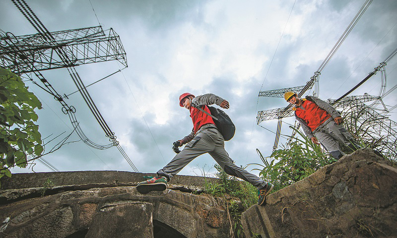 特高壓密集通道多處于山區(qū)，地理環(huán)境復(fù)雜，植被茂密，山火頻發(fā)，一旦發(fā)生線路同跳，將直接危及華東電網(wǎng)的安全。近日，天氣炎熱，用電負(fù)荷攀升，特高壓線路密集通道的運維也迎來了一年中最緊張的時期。圖為巡檢過程中，工作人員跨過山溝。