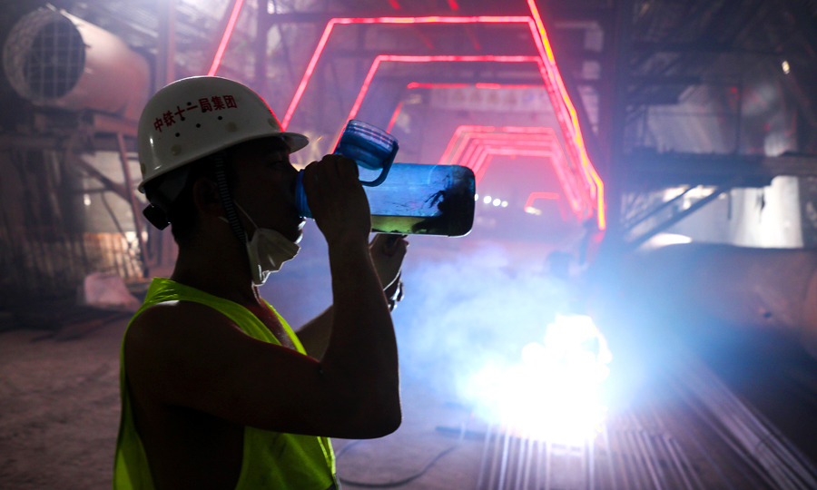 中鐵十一局與中鐵二十五局高度重視環境保護，隧道內放置多臺污水凈化設備對施工排水進行過濾處理，確保排水無害排放，兩臺灑水車對施工路段進行全天不間斷灑水降塵。引入隧道現場氣候環境實時監測系統，做到環保與施工同步推進。圖為隧道內外溫差30余度，施工人員正在補充水分。（鄒飛 攝）