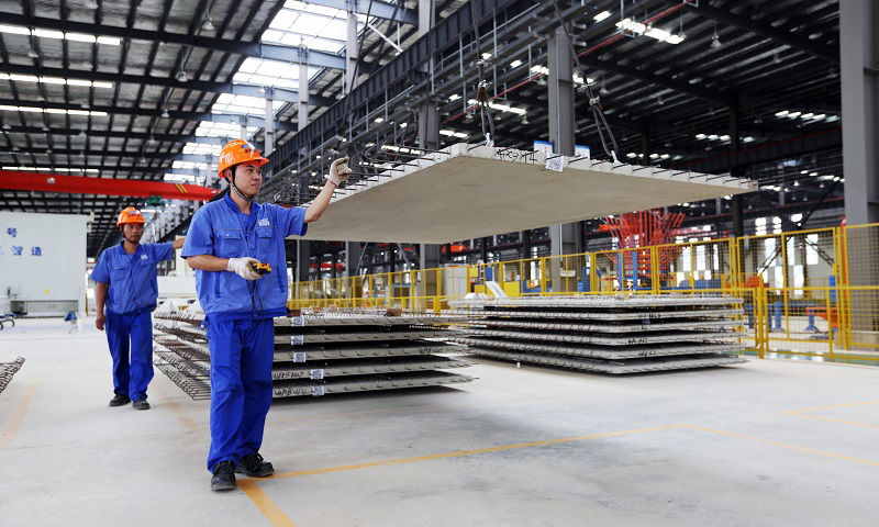 圖為建筑工人通過(guò)機(jī)械化作業(yè)，將一塊塊“樓板”運(yùn)送至運(yùn)輸車(chē)上。