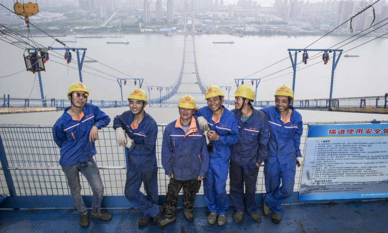 武漢楊泗港長江大橋施工現場，位于200多米高的“云端”。這是近80名中鐵大橋局工人日夜奮戰的陣地。他們穿梭在南北兩岸的貓道上，完成主橋主纜架設和引橋承臺、墩身、箱梁施工。滾滾長江的上空，一條優美的“天梯”緩緩鋪開。圖為6月8日，中鐵大橋局工人溫遠科、馮奎、胡貴明、陳飛、耍惹日布、賴仕良在南岸施工平臺上的合影。（新華社記者 肖藝九 攝）