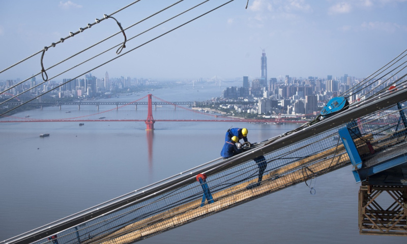 6月25日，來自四川瀘州的34歲工人劉能（右）與工友在高空作業。他們的后方依次是鸚鵡洲長江大橋、武漢長江大橋、武漢長江二橋和武漢二七長江大橋。（新華社記者 肖藝九 攝）