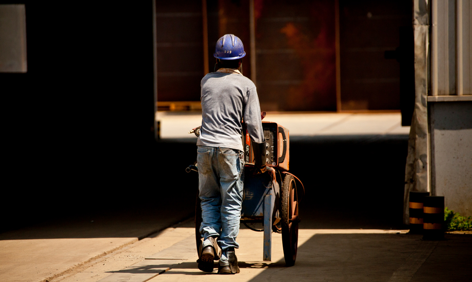 盡管室外氣溫已達38攝氏度，因為安全防護需要，中鐵四局鋼結構建筑公司制造分公司的作業工人也必須把自己從頭到腳防護起來。汗水從帽子和眼鏡的縫隙里流淌下來。每個工位都有不停轉的風扇，每個工人都有超大容量的水杯。每年他們都要經歷百十來個這樣難熬的高溫工作日。（作者：朱曉晨）