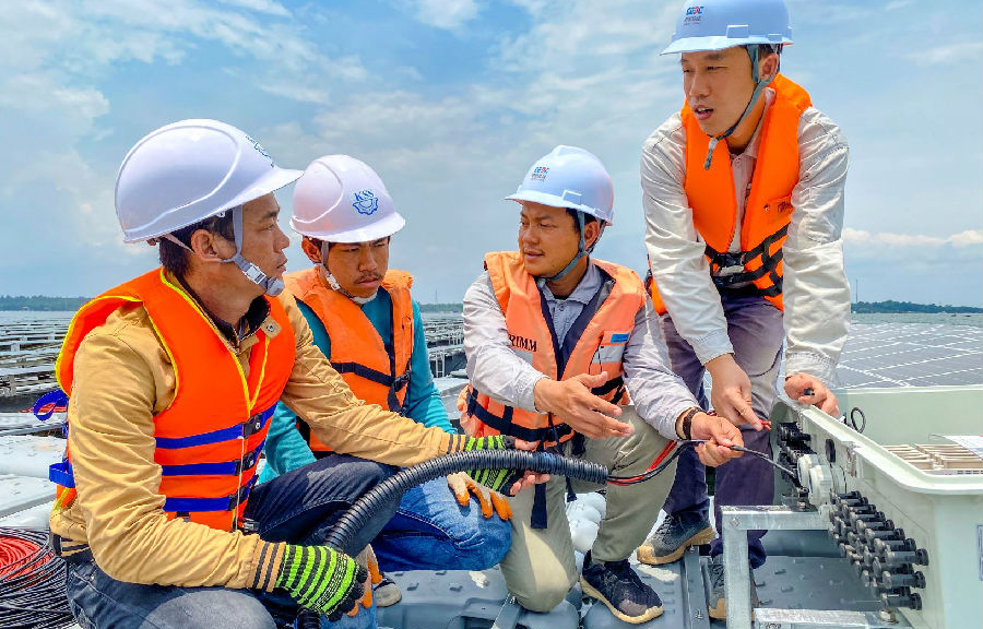 “五一”前夕，中國能建的項目建設工地一片繁忙，有序作業的建設者奮勇爭先，以飽滿的熱情迎接“五一”國際勞動節的到來。為確保工程穩步推進，“五一”期間，中國能建的建設者將全力以赴，奮戰在施工現場。圖為近日，在泰國詩琳通大壩漂浮光伏項目現場，安徽電建二公司技術人員向當地施工人員講解電纜接入的安裝流程與技術要點。