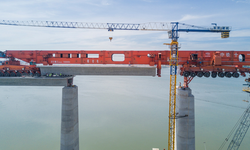 圖為7月11日，在新建福廈鐵路湄洲灣跨海大橋建設(shè)現(xiàn)場，中鐵十一局工人協(xié)同“昆侖號”千噸級運架一體機(jī)架設(shè)該線路最后一孔40米箱梁。（新華社記者 宋為偉 攝）