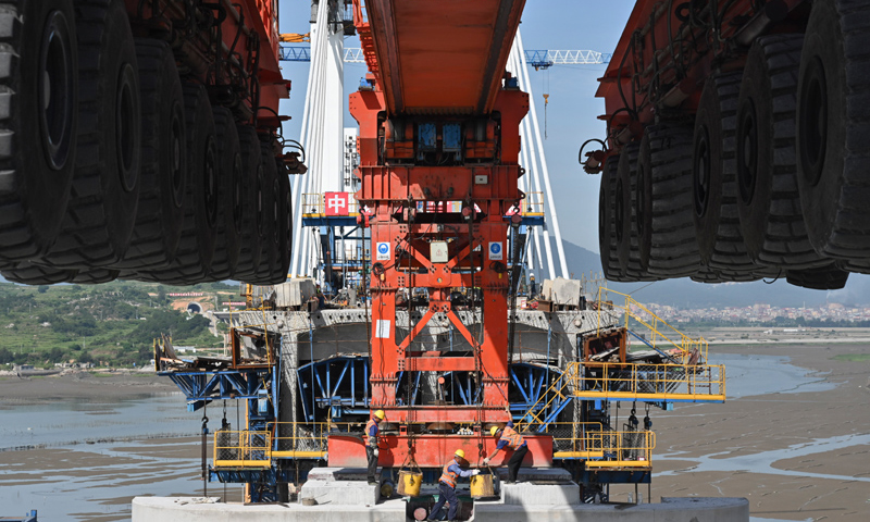 圖為7月11日，在新建福廈鐵路湄洲灣跨海大橋建設(shè)現(xiàn)場，中鐵十一局工人協(xié)同“昆侖號”千噸級運架一體機(jī)架設(shè)該線路最后一孔40米箱梁。（新華社記者 宋為偉 攝）