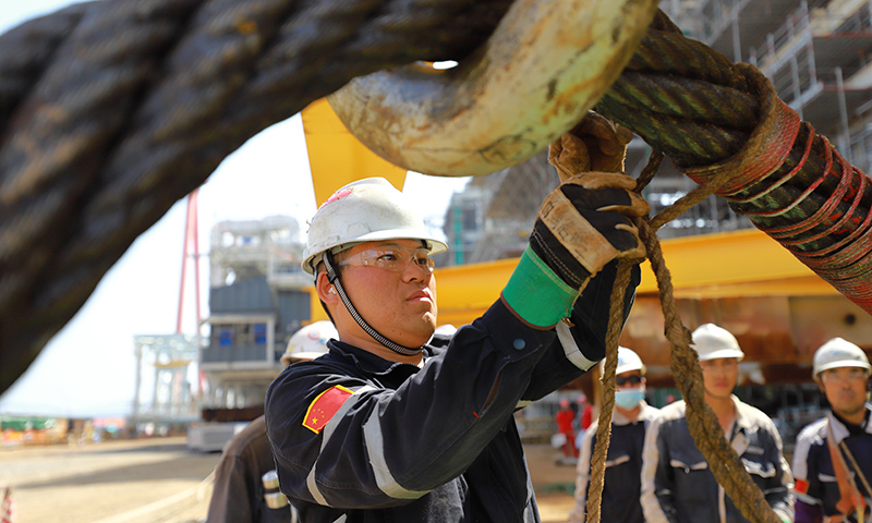 今年上半年，加拿大LNG項(xiàng)目第2列進(jìn)入場(chǎng)地總裝階段，伴隨著各模塊甲板片預(yù)制工作的全面展開(kāi)，場(chǎng)地及各類施工資源的緊張情況與日俱增，滑道之間原本寬闊的運(yùn)輸車道經(jīng)?！岸萝嚒?。圖為Mini E-House（電氣間）吊裝前，作業(yè)人員檢查繩扣是否牢靠。