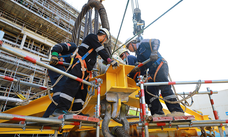 為有效緩解這一局面，高效推動(dòng)項(xiàng)目施工進(jìn)度，建造事業(yè)部青島公司在提升精細(xì)化管理能力和水平上下功夫。通過(guò)成立甲板片臨時(shí)倒運(yùn)小組，提前疏通車道障礙，讓原本滯緩的場(chǎng)地運(yùn)輸工作高效運(yùn)轉(zhuǎn)。圖為Mini E-House（電氣間）吊裝作業(yè)人員合力安裝吊裝鎖具。