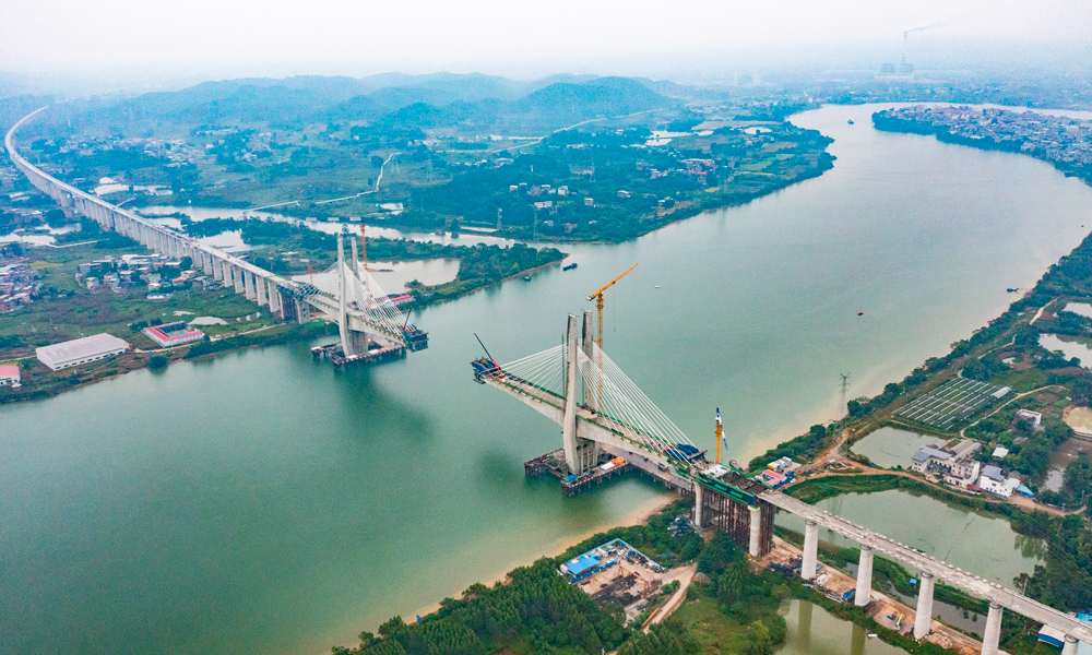 該特大橋鋼混結(jié)合段單側(cè)懸臂施工長15米，由2.7米長混凝土梁和12.3米鋼梁組成，懸灌重量為1800噸，由于鋼混段施工位于航道中間，需要采用懸吊施工工藝。建設(shè)團(tuán)隊(duì)創(chuàng)新思路方法，將鋼梁分為4.65米和7.65米兩次吊裝，再進(jìn)行混凝土分段澆筑的施工工藝，解決超長、超重鋼混段懸灌施工難題。圖為施工現(xiàn)場航拍中景。