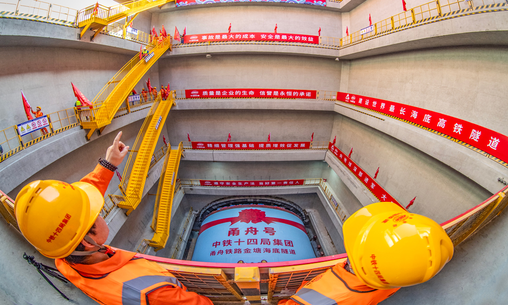 甬舟鐵路西起寧波東站，經(jīng)寧波市鄞州區(qū)、北侖區(qū)，終至定海區(qū)白泉鎮(zhèn)，線路全長約76.4公里，設(shè)計時速250公里，是一條以中長途旅游客流為主、兼顧舟山寧波之間城際客流的高速鐵路。金塘海底隧道西起寧波市北侖區(qū)，東至舟山市金塘鎮(zhèn)，全長16.18公里，其中盾構(gòu)段長11.21公里，穿越金塘水道，“甬舟號”和“定海號”兩臺盾構(gòu)機相向掘進(jìn)至海底穩(wěn)定巖層區(qū)間“會師”后拆解，是甬舟鐵路全線控制性工程，也是目前世界最長海底高鐵隧道。圖為“甬舟號”盾構(gòu)機始發(fā)現(xiàn)場。