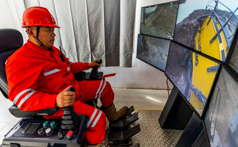 在準(zhǔn)能集團黑岱溝露天煤礦智能礦山建設(shè)現(xiàn)場指揮中心，700噸級液壓正鏟司機正在通過遠(yuǎn)程操控方式配合300噸級礦用無人駕駛卡車進(jìn)行裝車作業(yè)。該系統(tǒng)模擬駕駛艙真實駕駛環(huán)境，采集駕駛室內(nèi)真實聲場信息，輔以低延時、高帶寬的5G通信技術(shù)，對信號、圖像、數(shù)據(jù)和指令進(jìn)行傳輸，實現(xiàn)在辦公樓內(nèi)實時、精確遠(yuǎn)程控制液壓正鏟作業(yè)。李瑞榮 攝