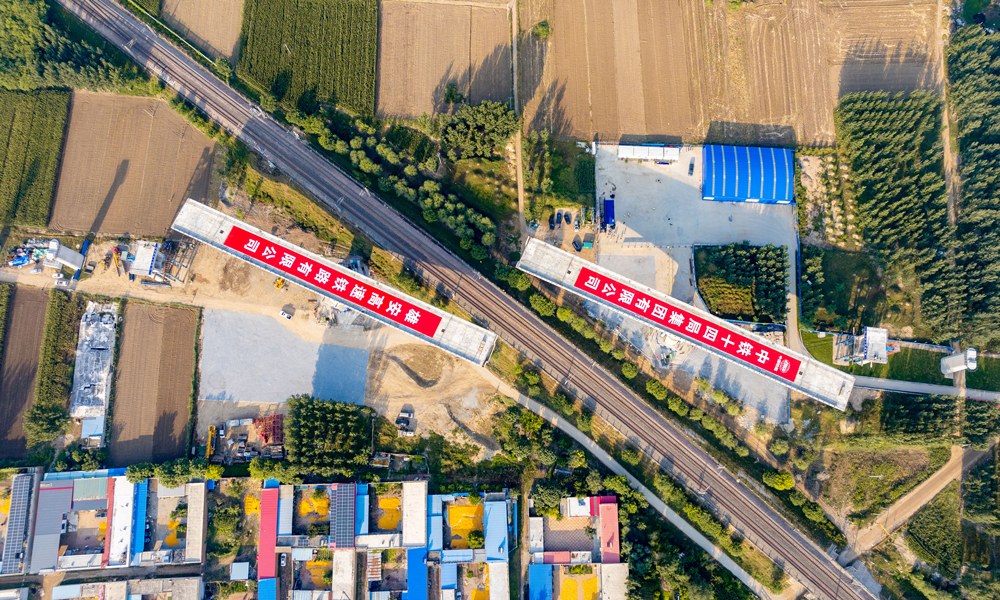 據(jù)介紹，任丘特大橋跨京九鐵路轉(zhuǎn)體橋是項(xiàng)目關(guān)鍵控制性工程，為雙幅結(jié)構(gòu)，單邊橋體長126米，橋面寬12.6米，重1.01萬噸，橋梁距離鐵路防護(hù)柵欄最小距離為9.5米，轉(zhuǎn)體后距鐵路接觸網(wǎng)垂直距離僅2.9米。施工過程中，對主梁線形控制、技術(shù)精度要求極高，安全風(fēng)險(xiǎn)較大。圖為任丘特大橋跨京九鐵路轉(zhuǎn)體橋正在轉(zhuǎn)體中航拍。