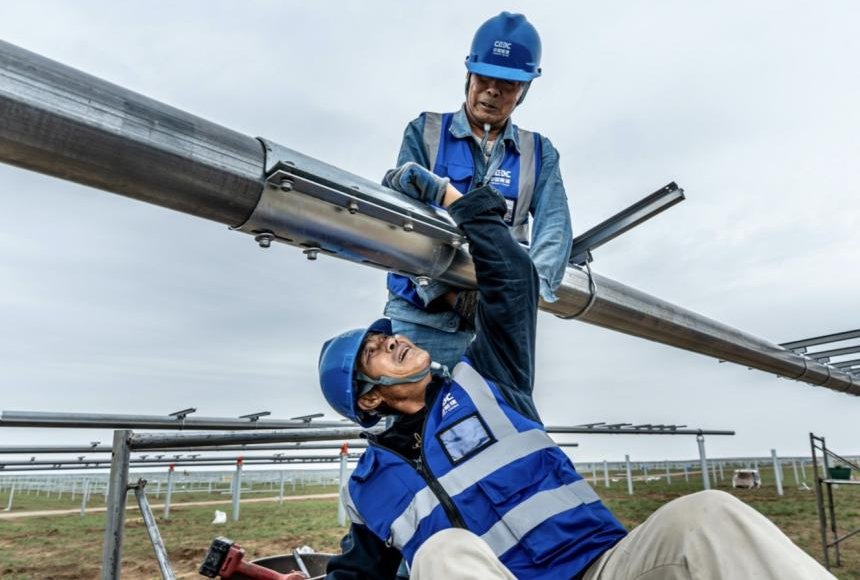 該項目在國內首次大規模應用平單軸H型鋼樁作為平單軸基礎，相比混凝土預制樁，打樁直徑從400毫米降至100毫米，顯著減少對草原地貌破壞。平單軸的應用可以實現光伏板追蹤太陽自動旋轉，大大提升發電效率。近4000名建設者分散在光伏基地各個作業面，他們不舍晝夜、日復一日的辛勤付出，讓這片荒涼的土地成功煥發生機，源源不斷向外輸送清潔能源。圖為建設者在緊固平單軸螺栓。