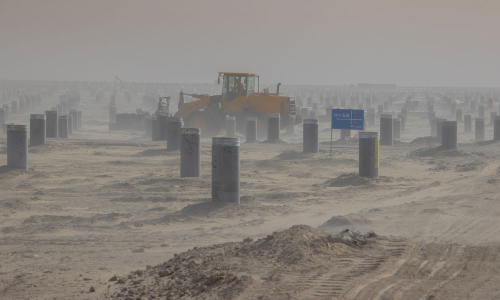 該項目作為塔里木油田公司目前施工的最大光伏發電項目，占地面積約2266公頃，南北、東西長寬均超過5公里。建設施工面廣線長，目前，已投入3500人到光伏面板架設、升壓匯集站及電化學儲能系統等建設工作，確保工程建設有序有效推進。圖為工程車輛在風沙中平整施工場地。 