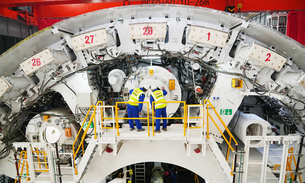 面對項目施工風險和難點，中鐵十四局項目團隊不斷創新攻關，通過增加刀具數量，加密刀具旋轉軌跡，配備高硬度、高韌性滾刀，以提高刀盤整體切削性能，同時配備刀盤刀具磨損自動監測功能、主驅動狀態監測系統、氣墊式泥水壓力平衡系統、同步雙液注漿系統等，對盾構機運行狀態進行連續監控，實現切口壓力的精準控制，保證及時調整機身姿態和同步注漿參數，實現盾構隧道沉降的毫米級精控。圖為技術人員在驗收盾構機。