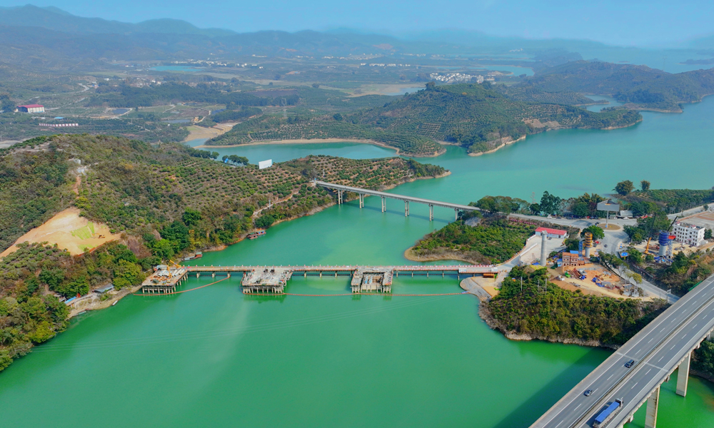 近日，由中鐵二十五局承建的黃百鐵路那蒙澄碧河特大橋樁基施工過半。當前正全力進行橋梁下部結構施工。該橋跨越的澄碧河水庫是國家一級飲用水源，也是國家保護野生動物中華秋沙鴨的越冬之地。為保護水源，建設團隊創新采用生態防護技術體系，結合云端水質監測系統實時預警污染風險，形成“物理隔離+智能防控”雙重保障。西黃百鐵路建成后將強化西南地區與“一帶一路”的陸海聯動能力，更好地服務新時代西部大開發。圖為那蒙澄碧河特大橋施工現場。