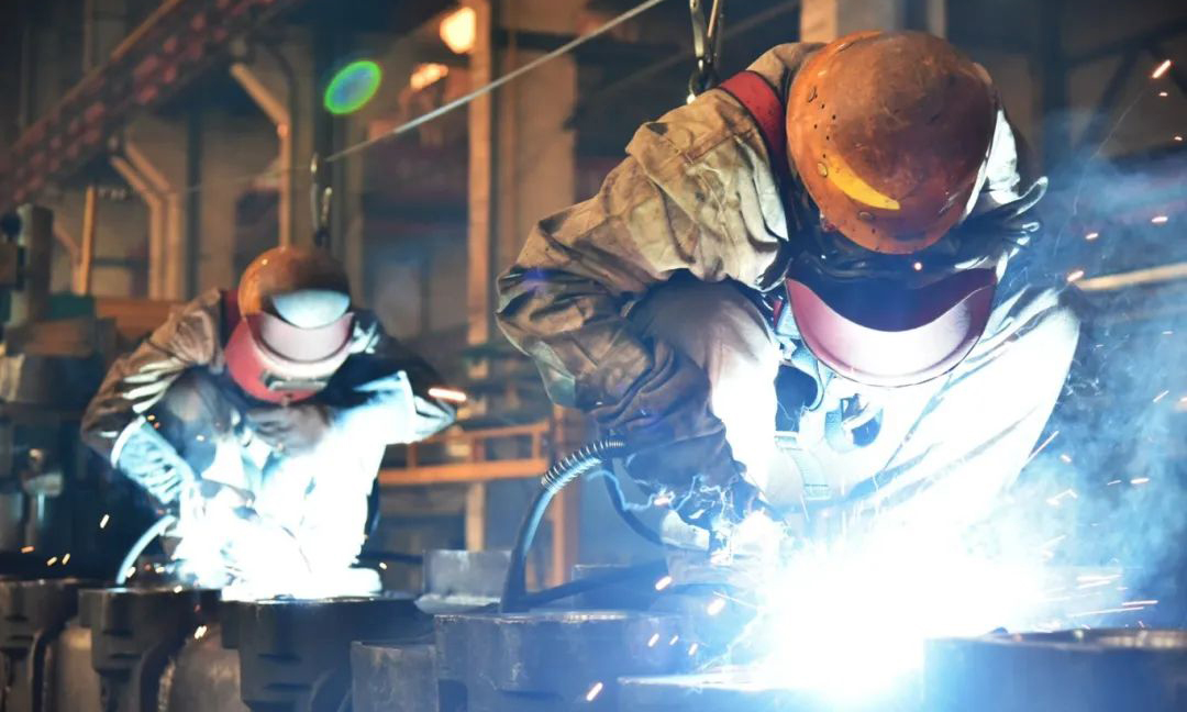 在一機集團裝焊車間生產(chǎn)一線，工作人員手握焊槍和焊帽在車體頂部進行高處焊接作業(yè)。