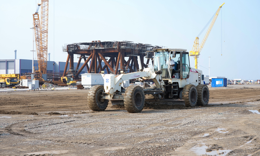 目前，該基地已為渤海油田多個項目開展單體、組塊建造服務，累計出貨噸數超8萬噸。據了解，二期項目投產后，該基地將形成包括平面分段生產線、工藝管線生產線、結構管線生產線、自動化立體倉庫在內的四大智能生產中心，總體設計產能可由3.3萬結構噸躍升至8.8萬結構噸。圖為在海油工程臨港智能制造基地二期工程項目現場，施工人員駕駛地面掛平機對總裝場地進行面層刮平作業。