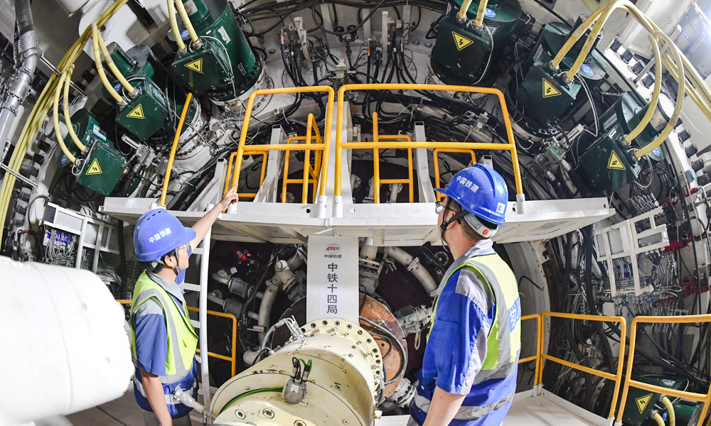 該隧道緊鄰海岸線，地下水位高、基巖起伏大、周邊建（構(gòu)）筑物密集，建設(shè)條件極其復(fù)雜，且盾構(gòu)隧道有1852米為淺覆土掘進(jìn)，最淺覆土僅為8.1米，沿線穿越上軟下硬、軟硬不均、孤石和基巖凸起等復(fù)雜地層，中風(fēng)化花崗巖強(qiáng)度最大達(dá)到了134.34兆帕，盾構(gòu)掘進(jìn)姿態(tài)控制難，易造成“翹頭”風(fēng)險，還需應(yīng)對高層建筑物錨索、雙線隧道小間距等諸多施工難題，對盾構(gòu)機(jī)整機(jī)的適應(yīng)性和刀盤刀具的耐磨性提出了極高要求。圖為工程技術(shù)人員巡檢盾構(gòu)機(jī)運(yùn)行情況。 