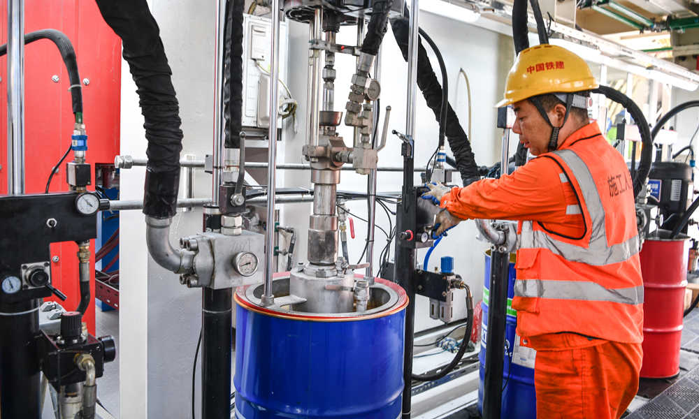 針對隧道施工風(fēng)險和難點(diǎn)，項目團(tuán)隊加強(qiáng)技術(shù)攻關(guān)，對“廈金號”盾構(gòu)機(jī)進(jìn)行針對性設(shè)計，配備了帶壓復(fù)合型刀盤，配置144把滾刀，增加刀具強(qiáng)度和旋轉(zhuǎn)軌跡，使刀盤整體切削性能和破巖效率得到顯著提升，還搭載了伸縮主驅(qū)動、同步雙液注漿、刀盤刀具磨損自動監(jiān)測、盾尾間隙自動測量、管片上浮自動測量、硬巖二次破碎等先進(jìn)智能掘進(jìn)和監(jiān)測裝置，同時運(yùn)用“智慧指揮中心”實(shí)現(xiàn)施工現(xiàn)場實(shí)時安全和信息化管控，確保隧道安全高效掘進(jìn)。圖為施工人員檢查油脂情況。 