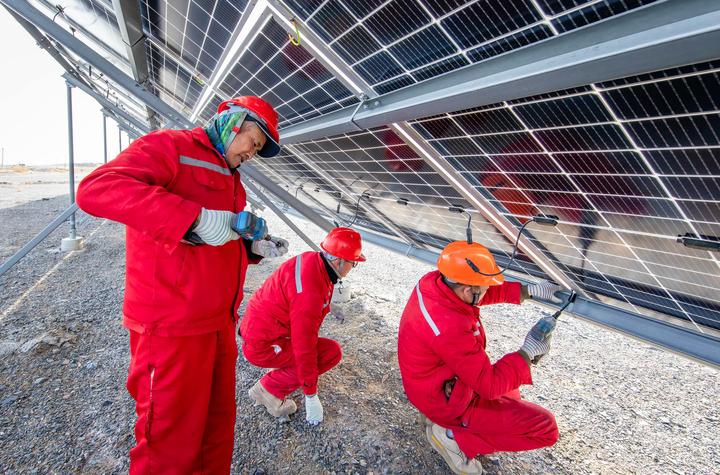 站在準噶爾盆地，放眼望去，光伏板陣列如同一望無際的藍色海洋，在微風中泛起層層“漣漪”。巡檢班工作人員踩著砂石地，認真細致地檢查每一塊光伏板。這是新疆油田推進綠色低碳轉型的關鍵所在。黑色的石油與藍色的光伏海洋，在這片土地上和諧共生，共同繪就了一幅別樣的能源發展畫卷。圖為新疆油田吉慶油田作業區新能源項目部工作人員維護太陽能光伏板。