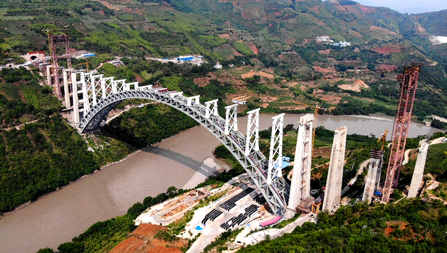 近日，隨著一塊重達(dá)120噸的鋼箱梁節(jié)段穩(wěn)穩(wěn)落在大橋拱上立柱上，標(biāo)志著世界跨度最大的鐵路拱橋——大瑞鐵路怒江特大橋進(jìn)入梁部施工階段。圖為航拍的大瑞鐵路怒江特大橋。