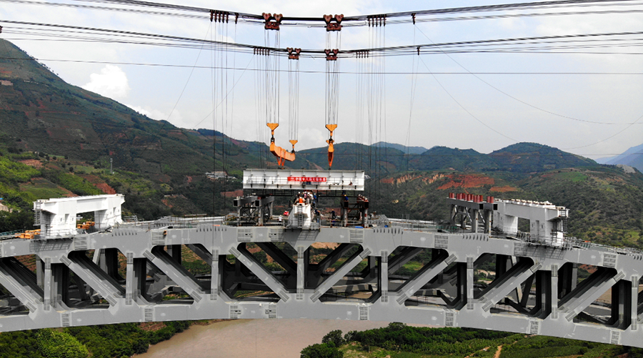 為保證大橋主拱穩(wěn)定性，降低施工風(fēng)險(xiǎn)，大橋梁部施工采用“吊裝+頂推”的施工方案。拱上鋼箱梁利用纜索吊吊裝，跨中五節(jié)段鋼箱梁采用“支架法”拼裝，然后以此五節(jié)段梁體為施工平臺(tái)，進(jìn)行剩余節(jié)段的焊接組裝，組裝成標(biāo)準(zhǔn)梁段后，采用纜索吊由跨中向兩側(cè)對(duì)稱吊裝，吊至相應(yīng)梁位后對(duì)位焊接。隨后，借助專用焊接平臺(tái)完成鋼箱梁環(huán)縫的焊接、補(bǔ)涂裝施工任務(wù)，利用檢修通道完成鋼箱梁塊體之間的高強(qiáng)螺栓施工工作。圖為鋼箱梁節(jié)段落位。