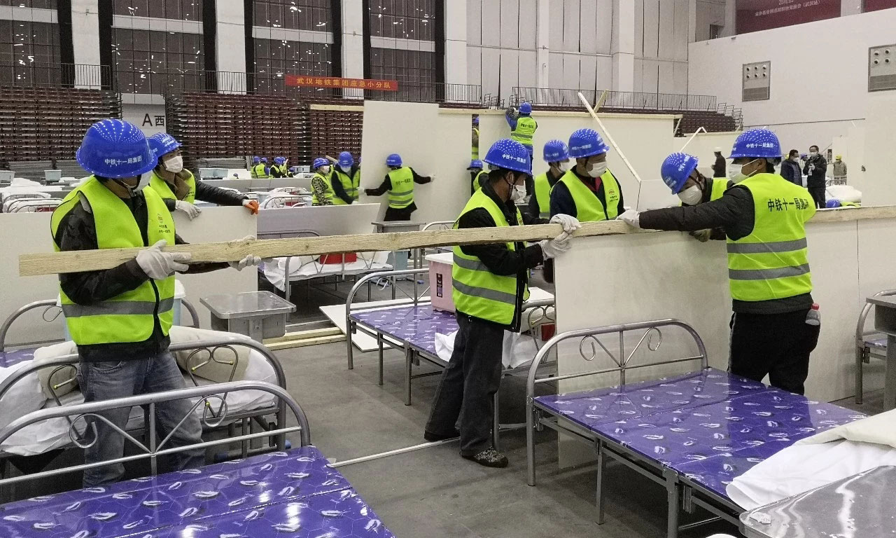 整個武漢客廳“方艙醫院”計劃在A、B、C三個廳布置2000個床位。此次增援主要負責武漢客廳“方艙醫院”A區12個倉位380多個病床隔板安裝、臨電安裝和門洞、吊頂、大門等施工任務。要求在最短時間內完成施工任務，為早日收治新冠肺炎病人贏得時間。圖為隔板安裝現場。