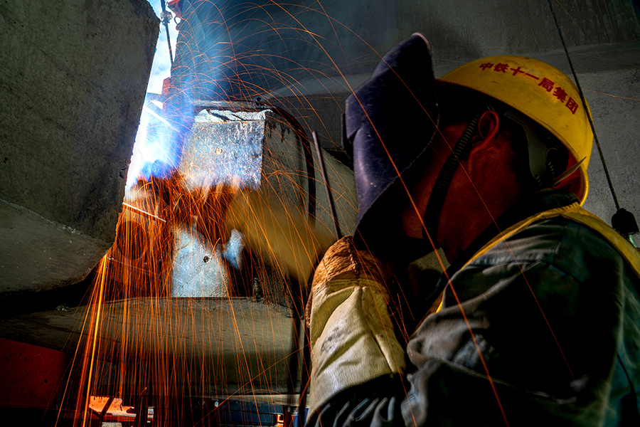 為降低此區域高空作業的風險，中鐵十一局三公司拉林鐵路鋪架項目通過科學組織、合理安排，先后對公路運梁車、公路架橋機進行了高原改造，增大了機械在橋面的固定面積，降低了架設時由于風速原因導致的安全隱患。圖為電焊工正在焊接橋梁連接板。（丁慶濱 攝）