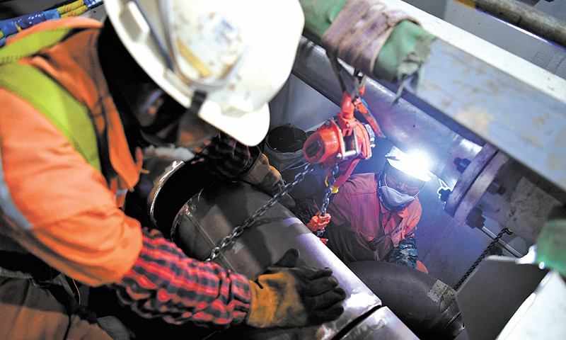 6月29日早7時許，滂沱大雨中，霧氣籠罩的中國海油青島場地上，陵水17-2半潛平臺船體四條“擎天巨臂”的最后一個“關節”完成吊裝。至此，我國首個1500米深水半潛平臺船體提前16天完成結構封頂，為船體陸地建造完工贏得了寶貴的時間。圖為船體內部，作業人員進行管線對接作業。