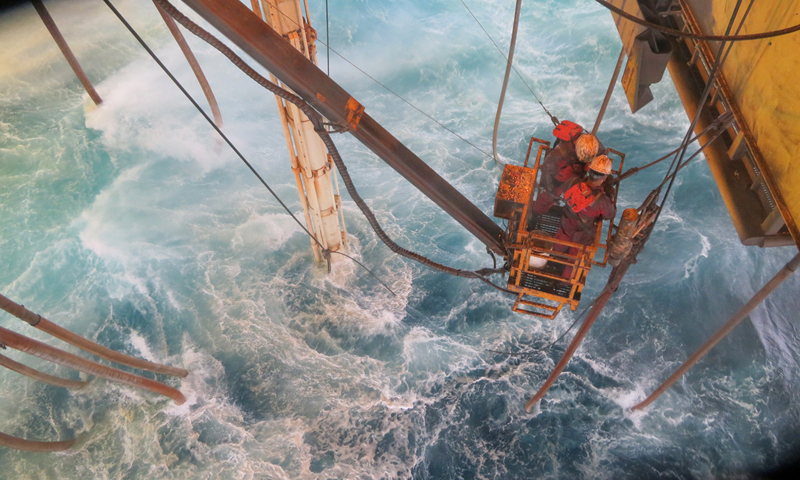 圖為“海洋石油982”鉆井平臺起防噴器作業中，員工在風浪中懸掛拆除鵝頸管，確保平臺順利起航避臺。
