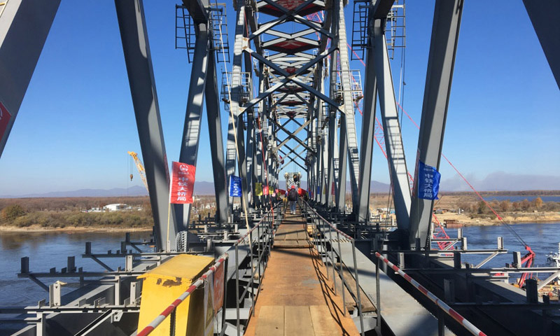 同江中俄鐵路大橋工程于2014年2月26日奠基，是中俄首座跨界河鐵路大橋，設(shè)計(jì)鐵路年過(guò)貨能力2100萬(wàn)噸。大橋全長(zhǎng)7193.71米，其中跨江大橋主橋全長(zhǎng)2215.02米，中方境內(nèi)1886.45米，俄方境內(nèi)328.57米。圖為10月13日，同江中俄鐵路大橋中方最后一吊鋼梁安裝到位。（新華社記者 王君寶 攝）